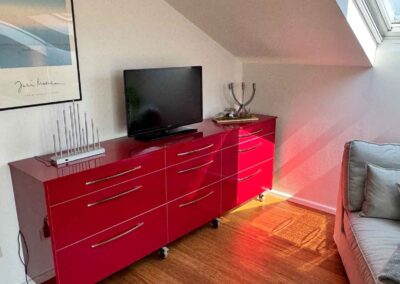 Detailaufnahme der roten Kommode im Haus Wohlfühlen - der Ferienwohnung in Ascheberg mit TV-Gerät