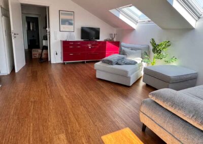 Auf der breiten roten Kommode ist das TV-Gerät platziert. Optimal um im Wohnraum vom Sofa und sogar von der Tischgruppe aus gut gesehen zu werden.