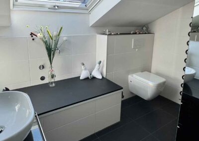 Das Bad der Ferienwohnung Haus Wohlfühlen in Ascheberg ist modern mit weiß und schwarz. Dieses Bild zeigt einen Gesamtüberblick von Waschbecken, Toilette und Eingang zur begehbaren Dusche.