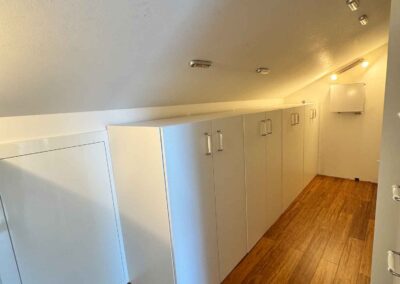 Es gibt viele Schränke in der Ferienwohnung Haus Wohlfühlen in Ascheberg. Hier sieht man 4 doppelflügelige Schränke, nebeneinander aufgereiht, etwas 1 Meter hoch sowie eine Dachschräge die darüber beginnt und mit Leuchten ausgestattet ist.
