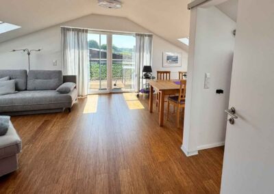 Wohnraum der Ferienwohnung Haus Wohlfühlen in Ascheberg im Münsterland zeigt den weiten Wohnraum mit Sofa, Sessel, Tischgruppe mit 4 Stühlen und den Blich zum Balkon